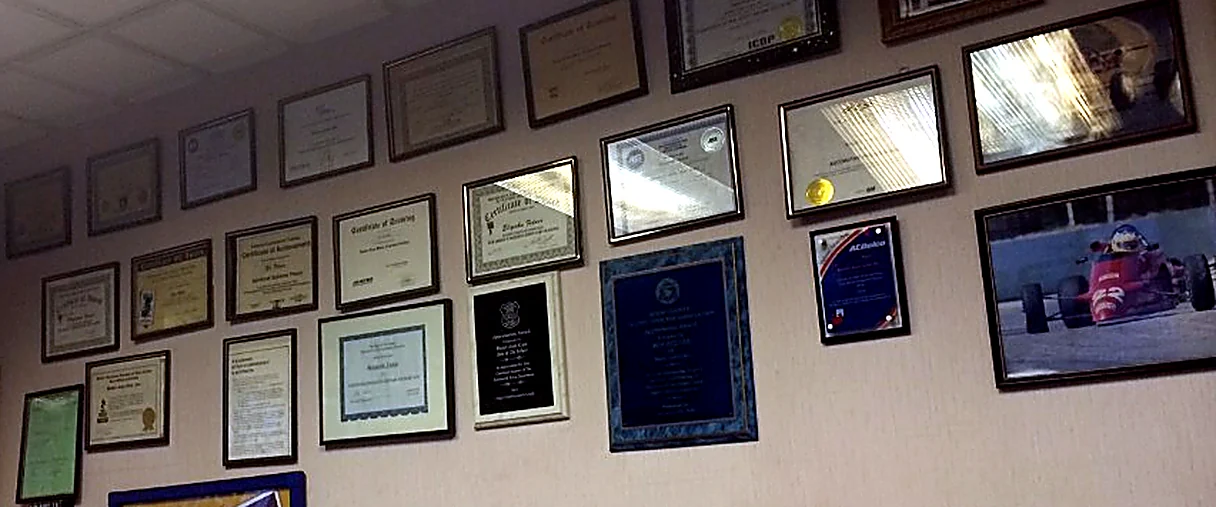 Framed training certificates, diplomas, and manufacturer plaques covering the office wall at Better Auto Care in Kenilworth, New Jersey